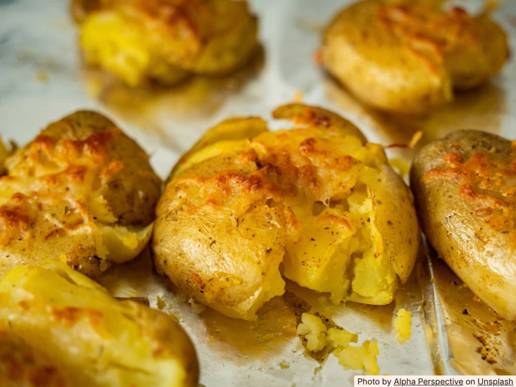 Hands pressing down on boiled potatoes on a baking sheet to smash them before roasting