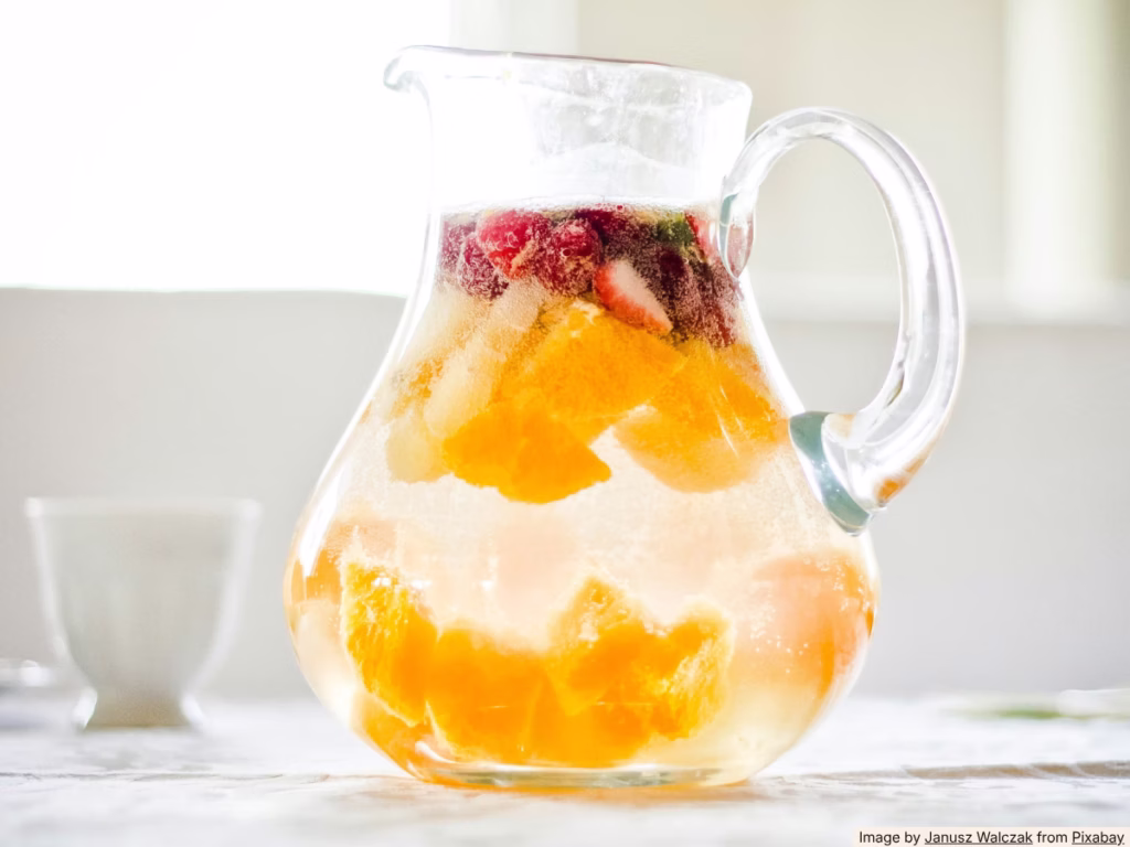 Glass of sparkling water with frozen berries and watermelon chunks as ice cubes on a sunny outdoor table