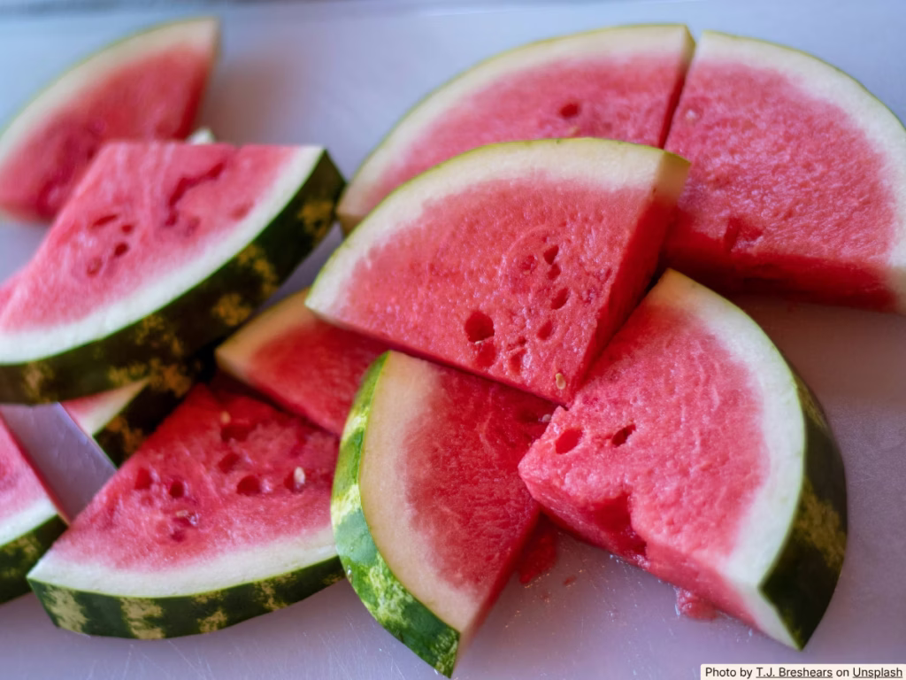 Whole watermelon on a wooden cutting board on a sunny outdoor table, ready to slice for a summer BBQ