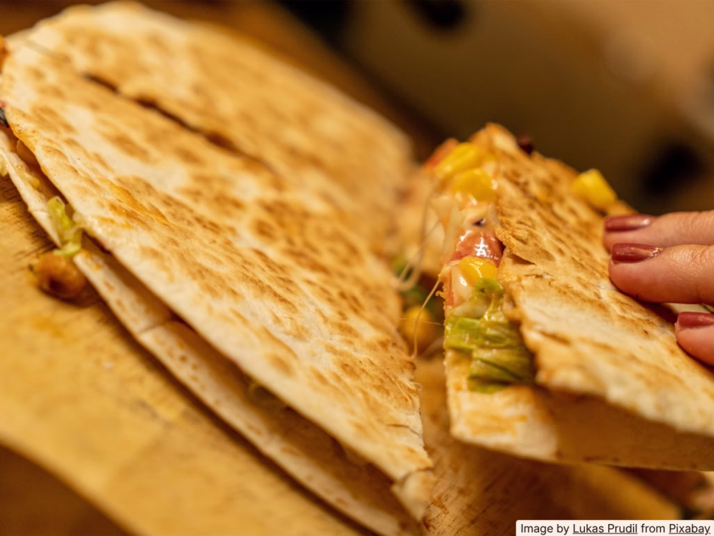 Leftover steak quesadilla cut in half on a wooden board, cheese pull visible, golden crust