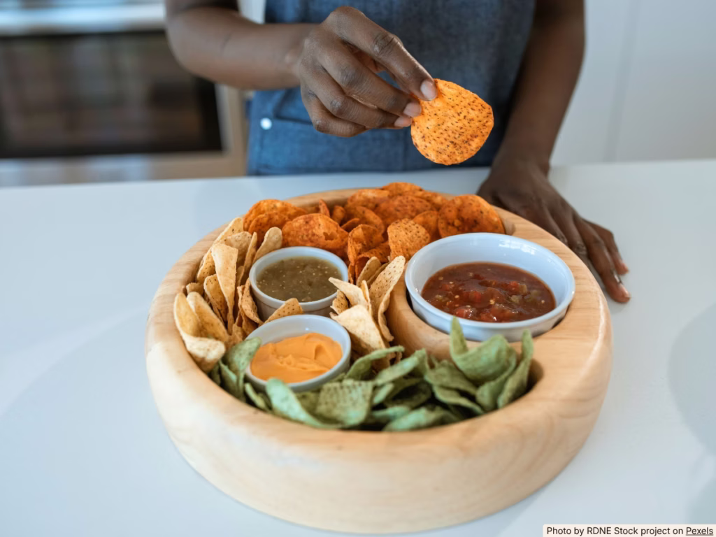 Hands scooping black bean dip with a tortilla chip at a casual snack spread