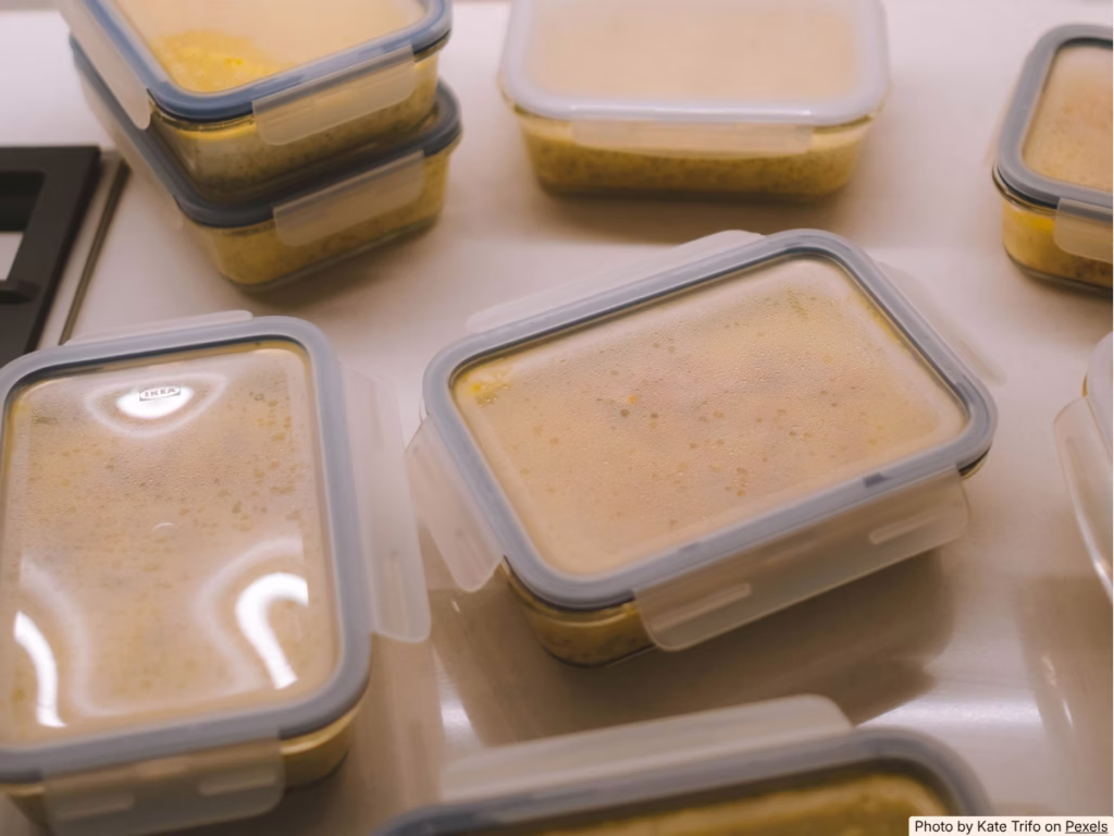 Open freezer drawer stacked with labeled square airtight containers of batch-cooked food