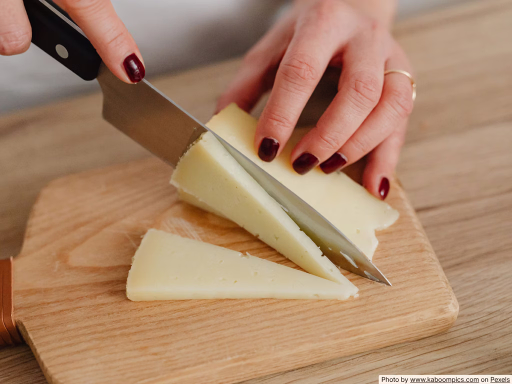 Hands cutting around mold on a block of hard cheese with a kitchen knife