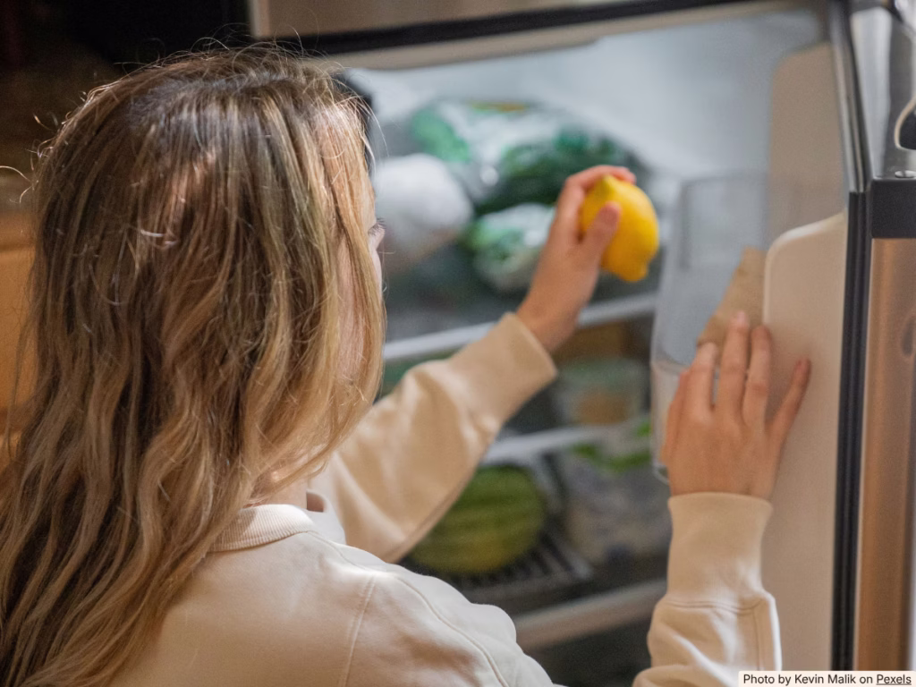 Hands pulling food items to the front of a refrigerator shelf during a pantry audit
