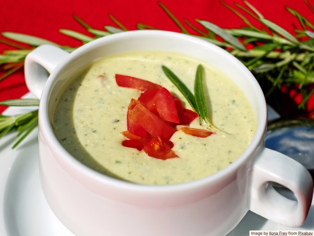 A pot of bright green zucchini soup on a stovetop with a ladle, warm kitchen light, batch cooking