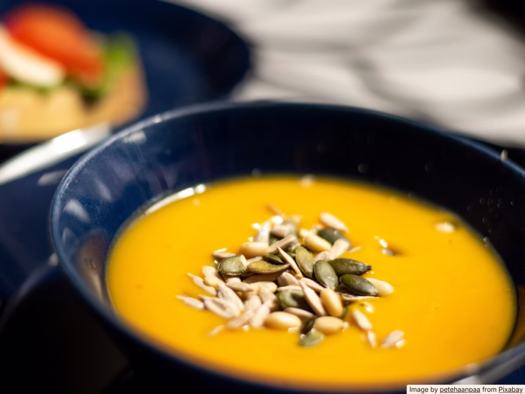 Small pot of creamy broth soup simmering on a stovetop with a wooden spoon resting on the rim