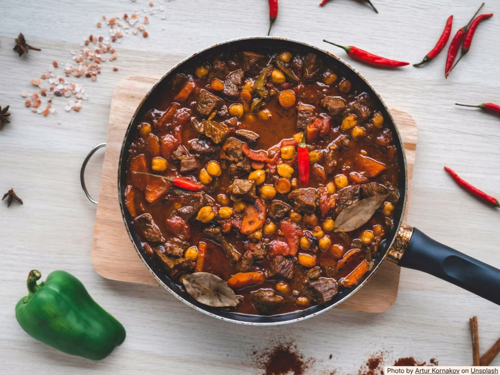 Large pot of chili simmering on a stove, the affordable anchor dish for a budget World Cup party for 10